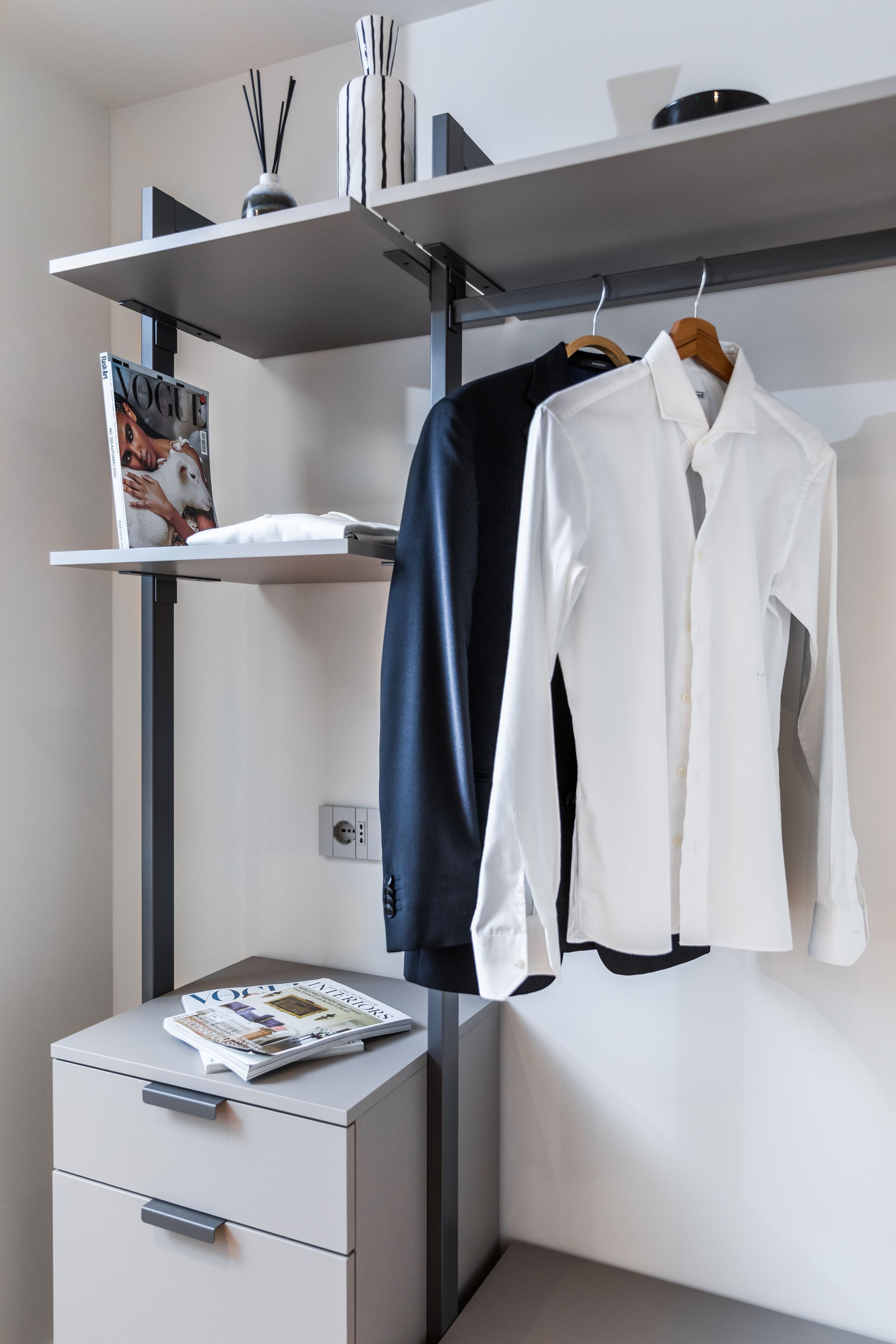 Une chambre moderne avec un placard intégré, un magazine posé sur une table d’appoint et un porte-manteau mural.