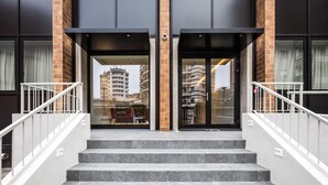 Entrada de un edificio con una escalera, una cámara de seguridad y un rascacielos al fondo.