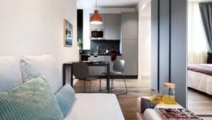 Una habitación de hotel moderna con sofá, una mesa de comedor con sillas, zona de cocina y cama.