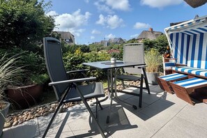 Ein möblierter Außenbereich mit Terrasse, Tisch, Stühlen, einem gestreiften Liegestuhl und einem Blumentopf.