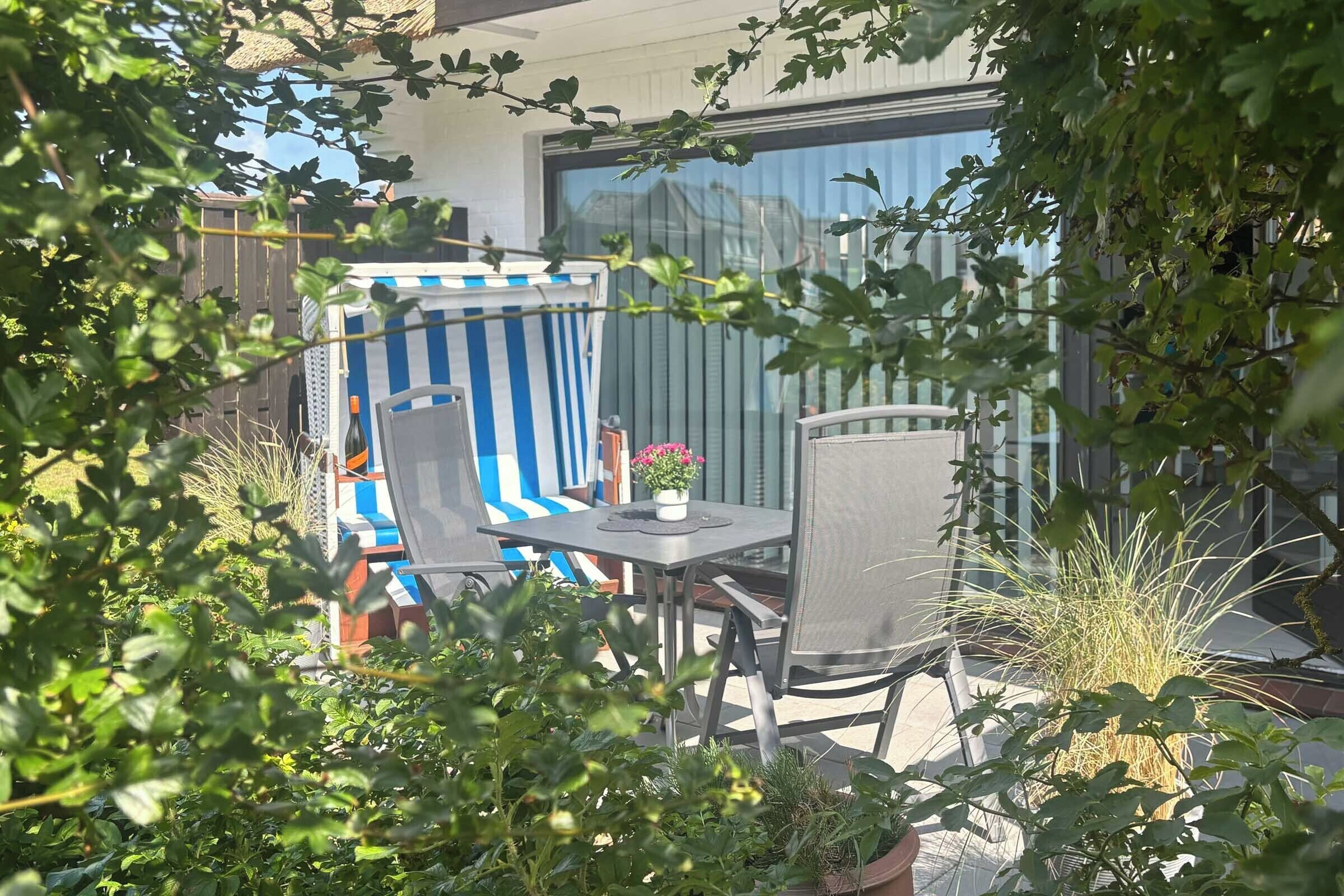 An outdoor seating area with a table and chairs, surrounded by potted plants and a striped chair.