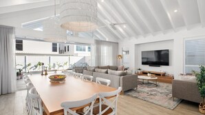A modern living room with a wooden dining table, white chairs, a grey sofa, and a flat-screen TV mounted on the wall. - Gone Coastal - Kingscliff (Kingscliff)