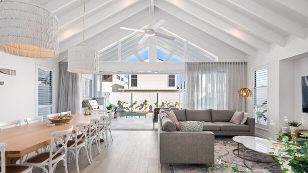 A spacious living area with a high ceiling, a dining table with chairs, a sofa, and a television. - Gone Coastal - Kingscliff (Kingscliff)