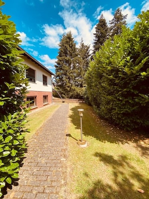 A pathway leading to a house with a brick facade and a white upper section. - Vacation apartment in the countryside on the edge of the Eifel National Park (Kommern)