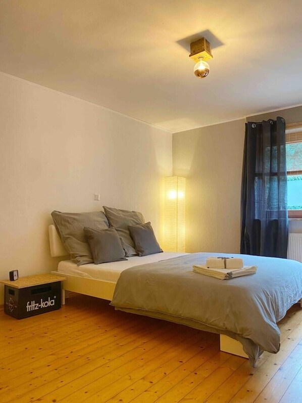 A bedroom with a bed, a bedside table, a lamp, and a window with curtains.