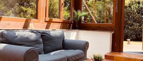A modern living room with a grey sofa, a small table with a plant, and a view of a garden through large windows.