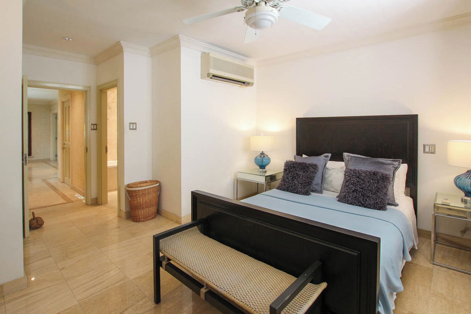 A bedroom with a bed, bedside tables, a bench, a ceiling fan, and an air conditioning unit.