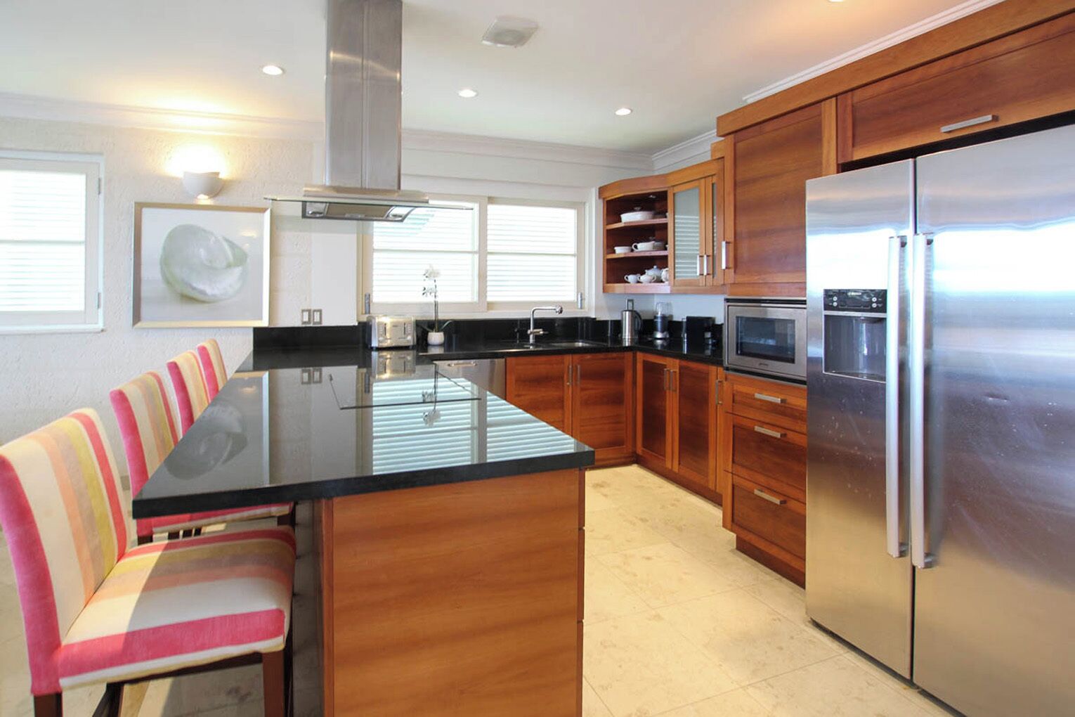 A modern kitchen with a central island, wooden cabinets, stainless steel appliances, and a seating area with striped chairs.