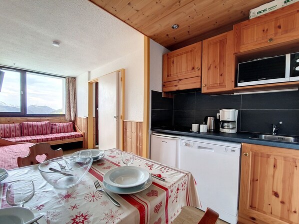 Una cocina acogedora con armarios de madera, microondas y lavavajillas. Una mesa de comedor está dispuesta con platos, vasos y cubiertos.
