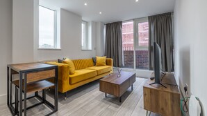 A modern living room with a yellow sofa, a wooden coffee table, and a TV on a wooden stand. - Stunning 2-bed Apartment in Camberley (Camberley)