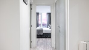 A narrow hallway leading to a bedroom with a bed, a window with curtains, and a radiator on the wall. - Stunning 2-bed Apartment in Camberley (Camberley)