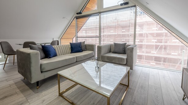 A modern loft-style living room with a large glass ceiling, a beige sectional sofa, a glass coffee table, and a view of the cityscape. - Impeccable 2-bed Apartment in Camberley (Camberley)