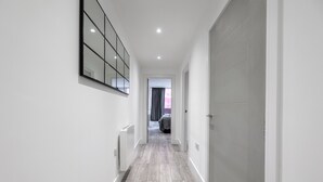 Un pasillo estrecho con suelo de madera, paredes blancas y un espejo grande a la izquierda.