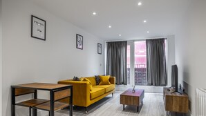 Una sala de estar moderna con un sofá amarillo, una mesa de centro de madera, un televisor sobre un mueble de madera y un cuadro enmarcado en la pared.