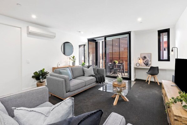 A modern living room with a grey sofa, a coffee table, and a TV stand.