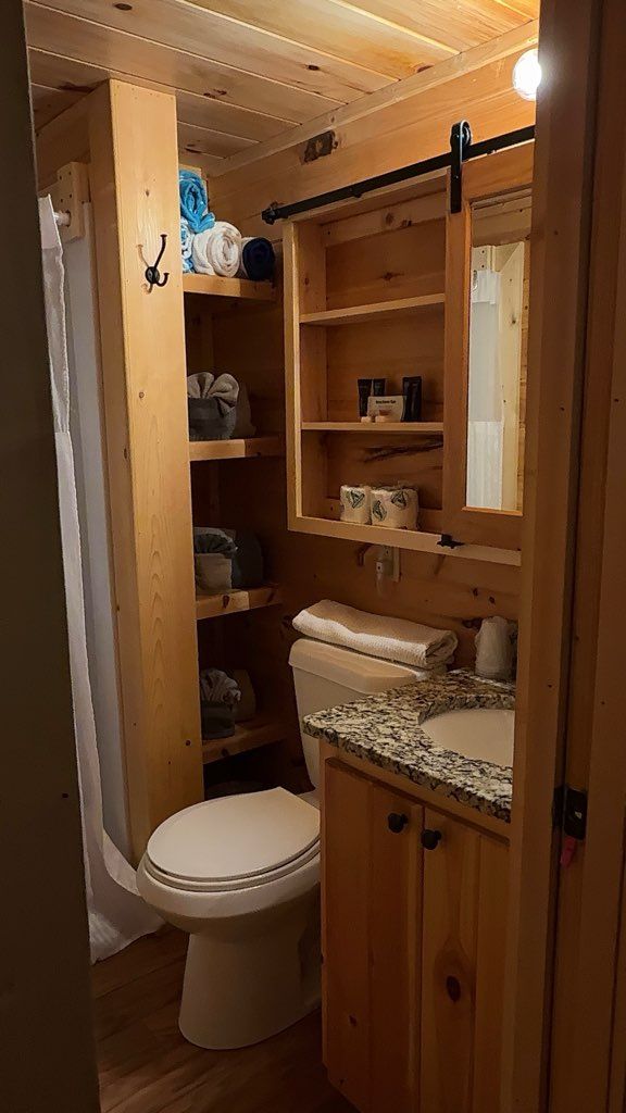 A wooden bathroom with a toilet, shelves, and a sink.