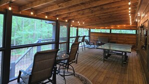 A wooden deck with tables and chairs, large windows, and string lights. - Copperhead Lodge and Resort Cabin Rentals (Blairsville)