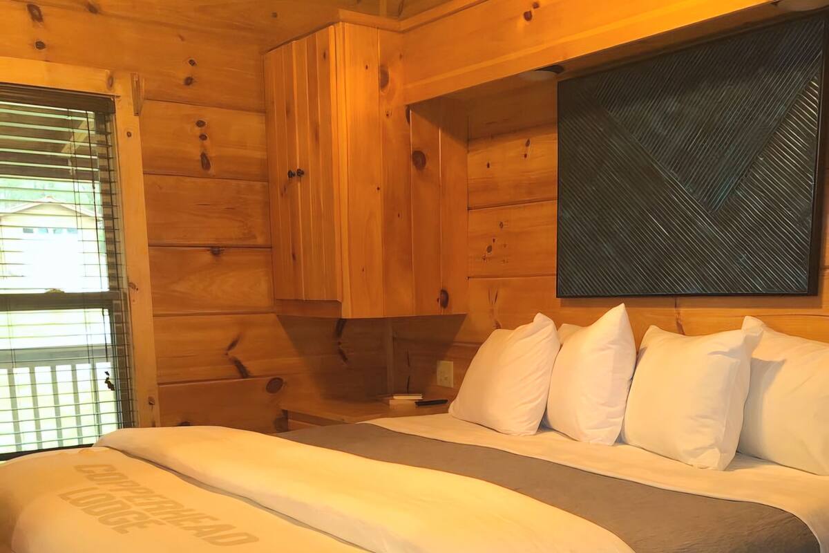 A wooden cabin-style bedroom with a bed, pillows, and a nightstand.