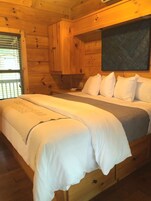 A wooden cabin-style bedroom with a bed, pillows, and a nightstand.