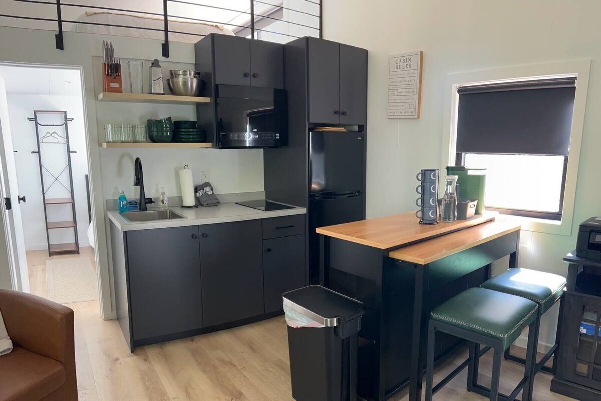 A modern kitchen with dark cabinets, a built-in microwave, and a small island with stools.