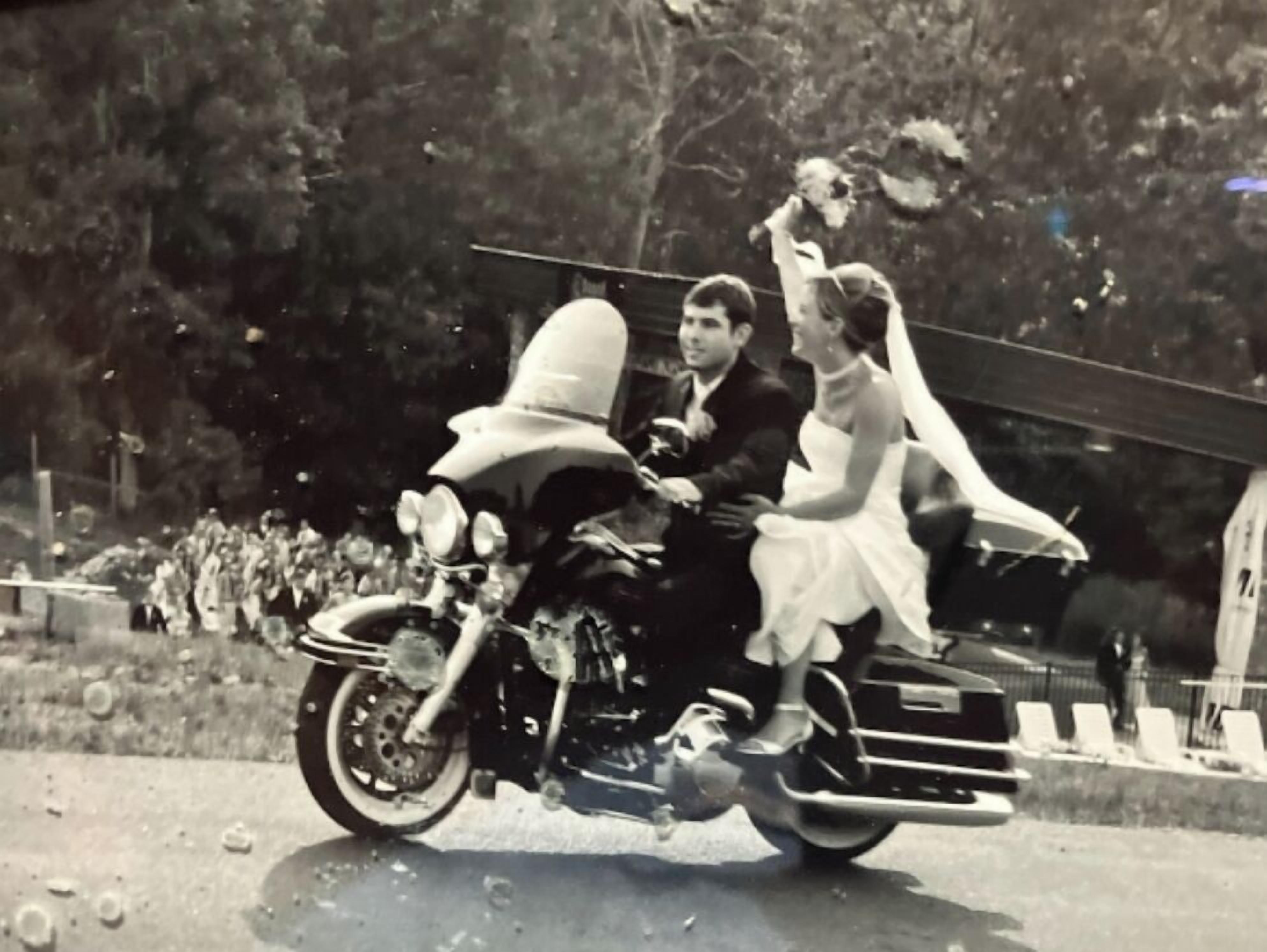 A vintage motorcycle with a sidecar, a bride, and a groom.