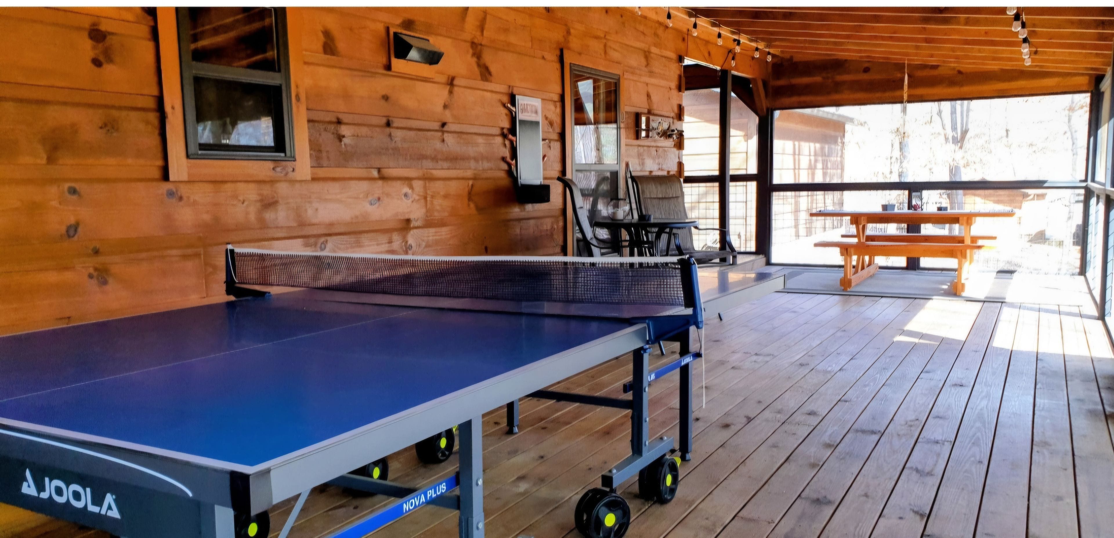Taula de ping-pong a l'interior d'una cabana de fusta, amb una taula i cadires al fons.