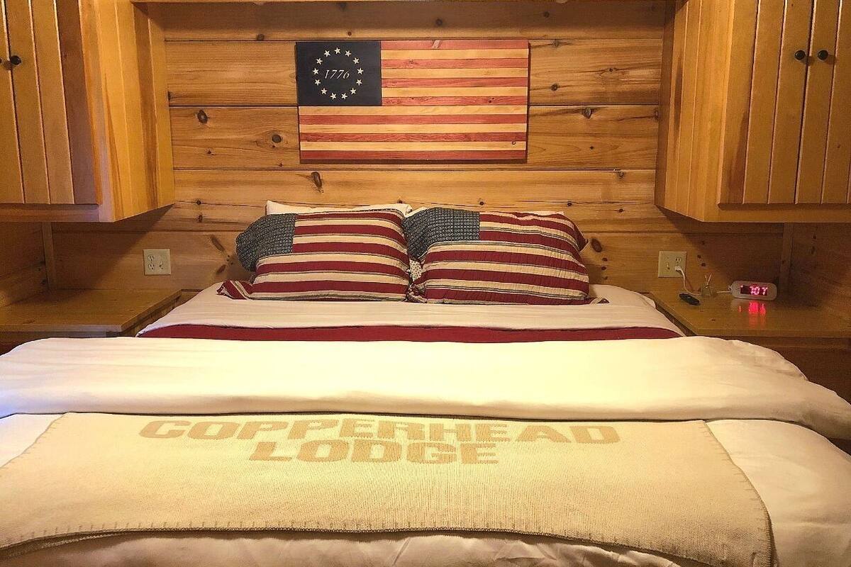 A wooden cabin room with a bed, pillows, a flag, and a clock.