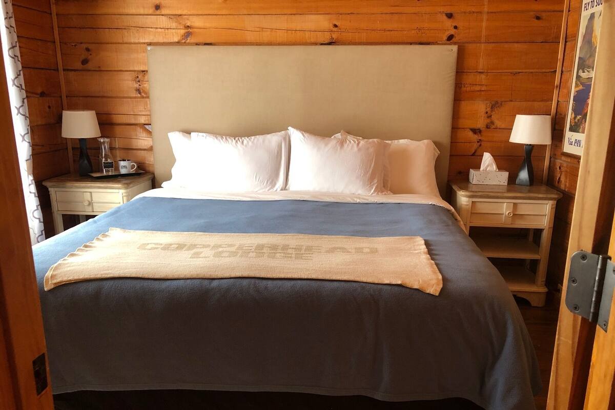 A wooden cabin-style bedroom with a bed, two bedside tables, and a nightstand.
