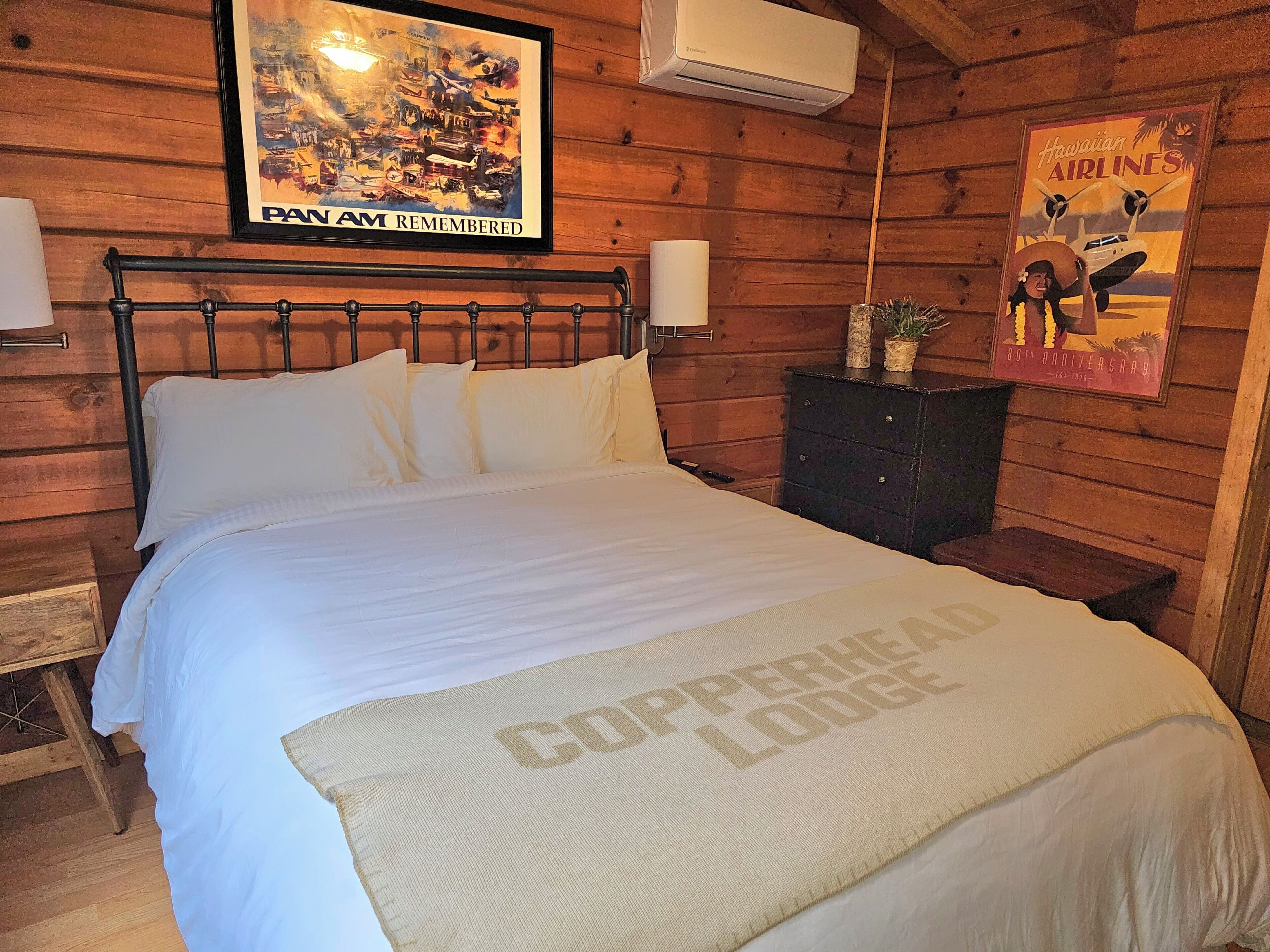 Una camera in stile baita di legno, con un letto, un quadro con un aereo d'epoca e un poster appeso al muro.