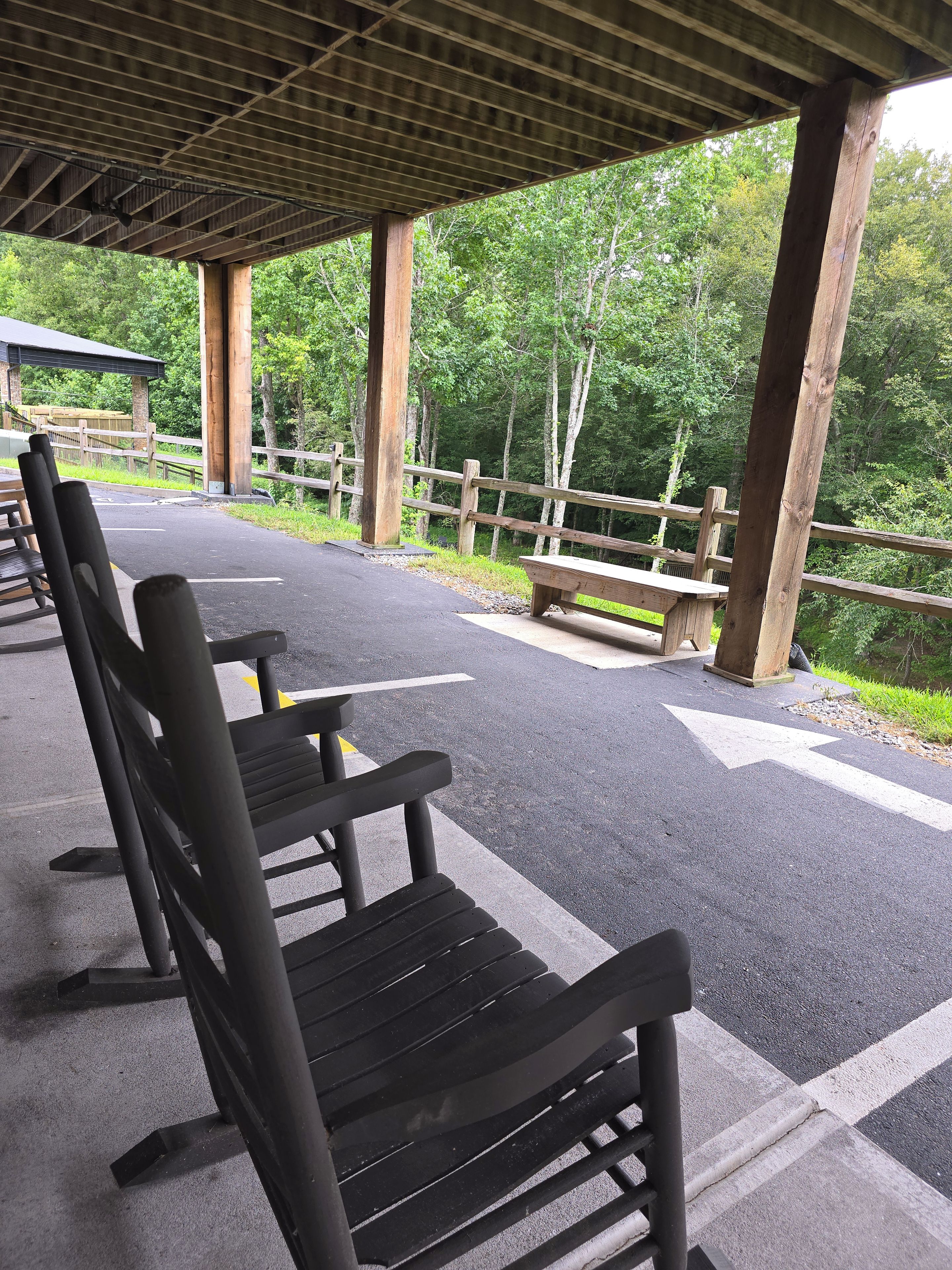 A covered picnic area with benches and tables, surrounded by a wooden fence and trees.