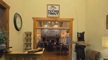 Interior de un restaurante con entrada de madera, un reloj, una decoración de oso y un cartel que dice 'The Flying Trout Restaurant'.