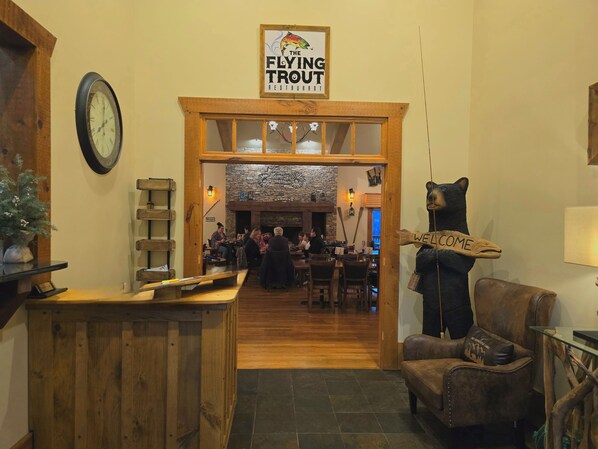 A restaurant interior with a wooden entrance, a clock, a bear decoration, and a sign reading 'The Flying Trout Restaurant.' - Copperhead Lodge and Resort Cabin Rentals (Blairsville)
