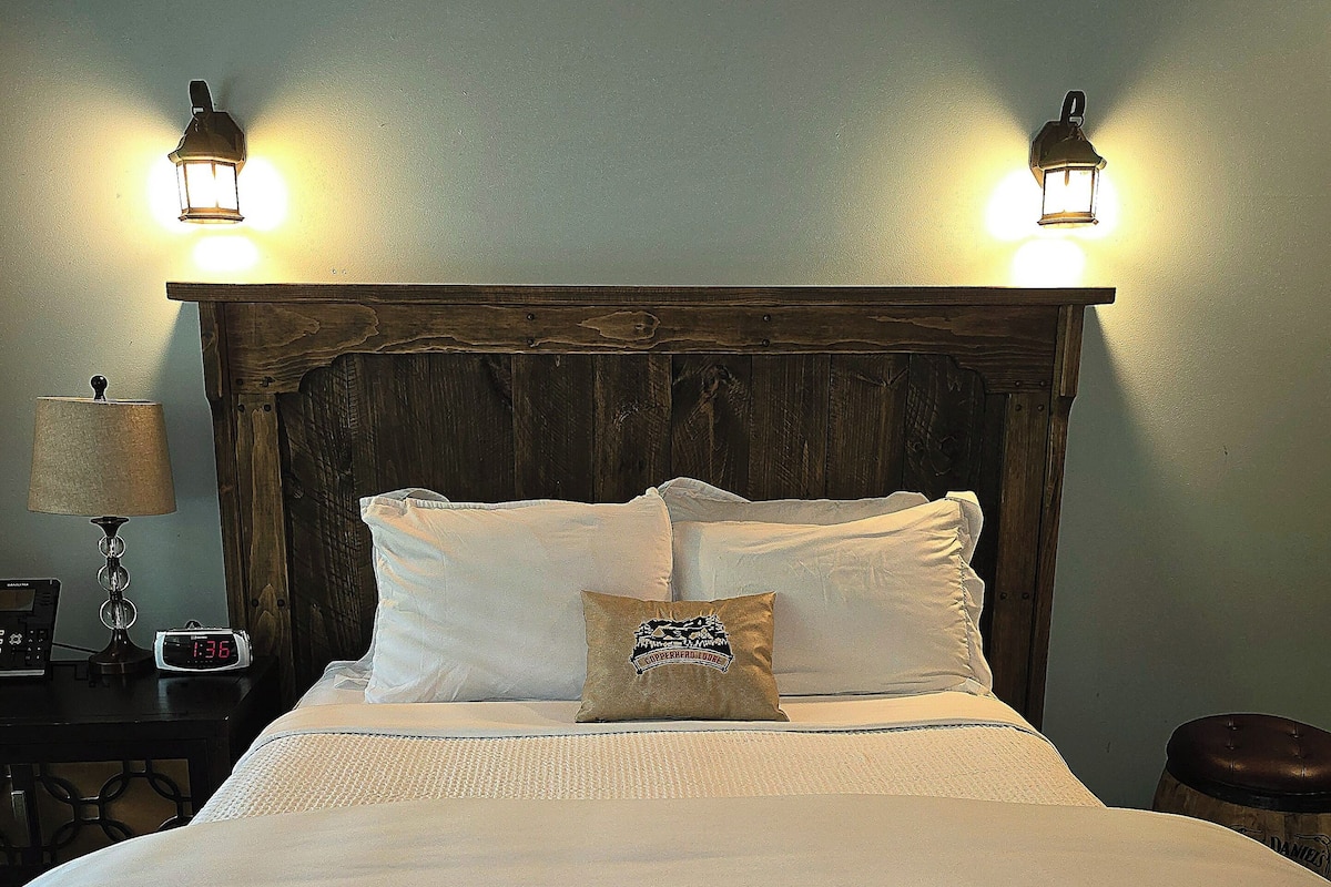 A neatly made bed with white linens and a decorative pillow, flanked by two wall-mounted lamps.