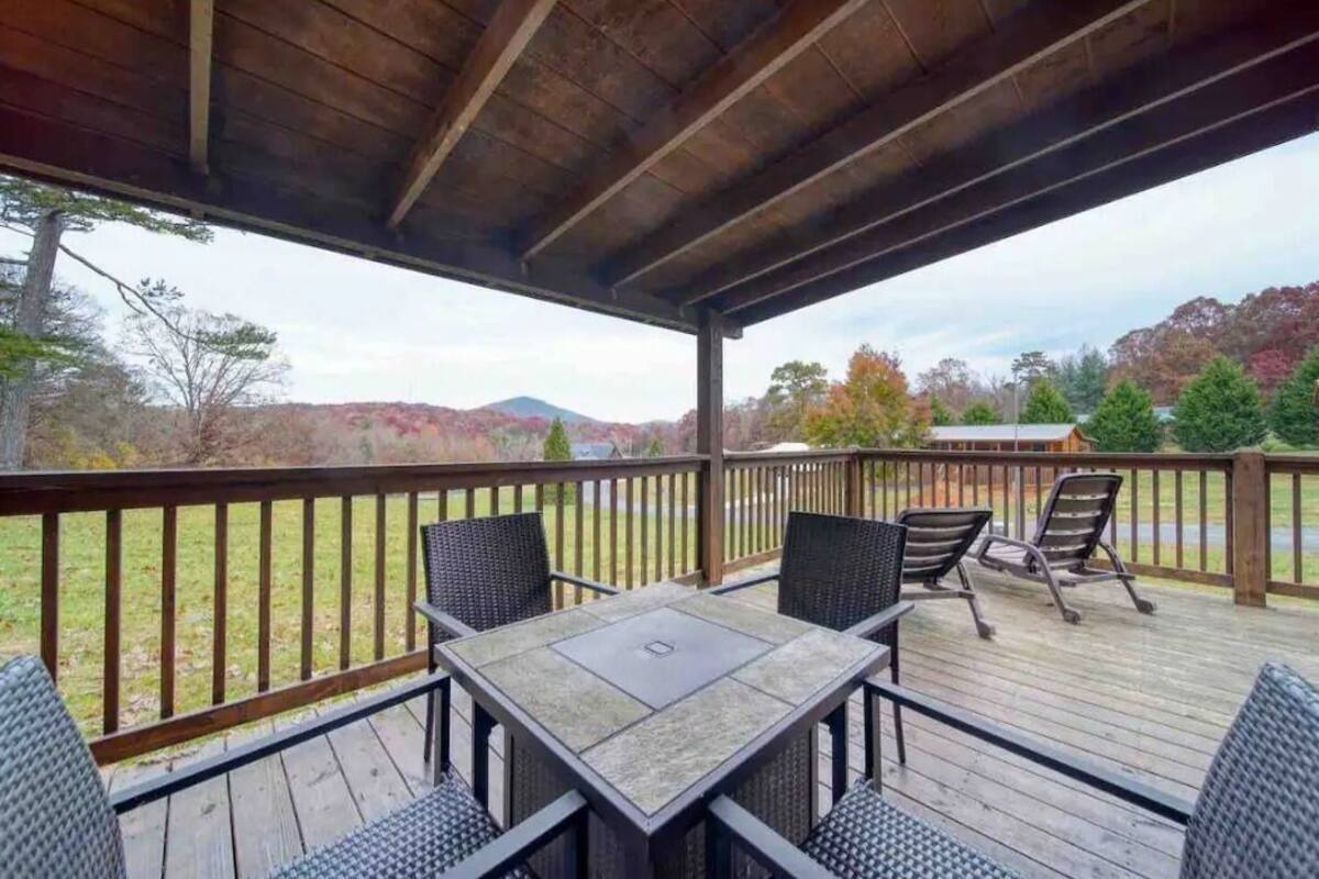 A covered outdoor deck with a table and chairs, overlooking a scenic landscape with trees and hills.