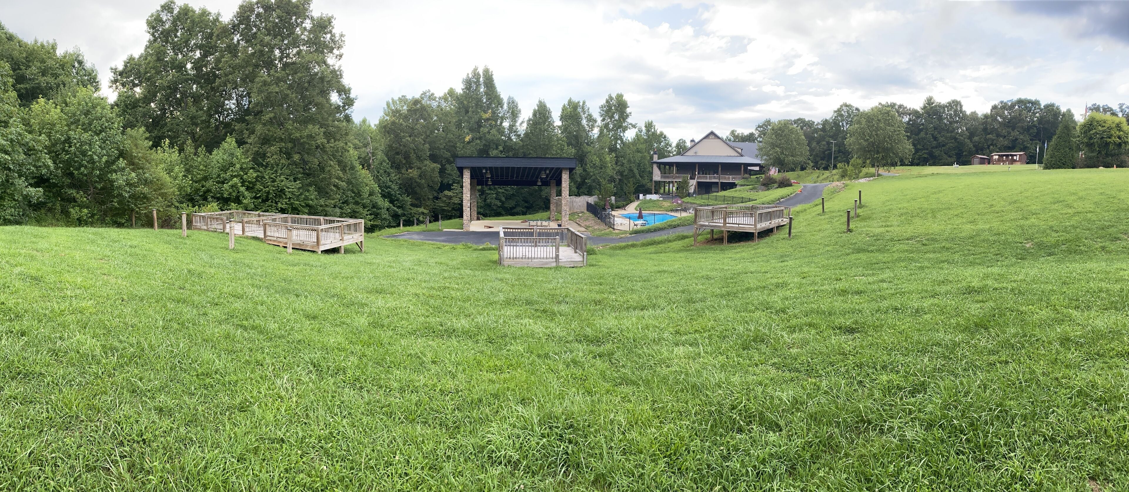 A grassy area with a pool, wooden decks, and a pavilion.