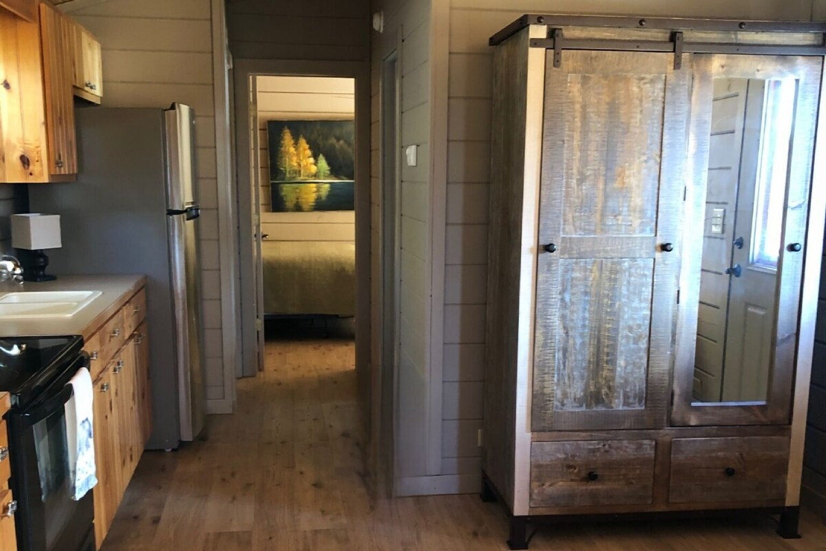 A compact kitchen with wooden cabinets, a refrigerator, and a dining area with a wooden table.