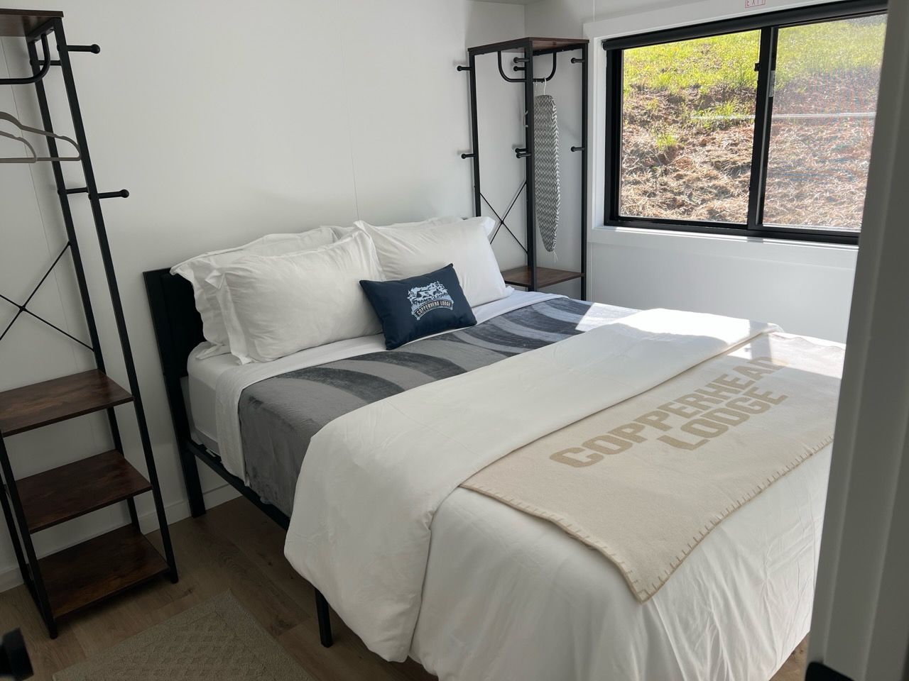 Une chambre à coucher avec un lit, une fenêtre, une étagère et un porte-objets fixé au mur.