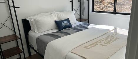 Une chambre à coucher avec un lit, une fenêtre, une étagère et un porte-objets fixé au mur.