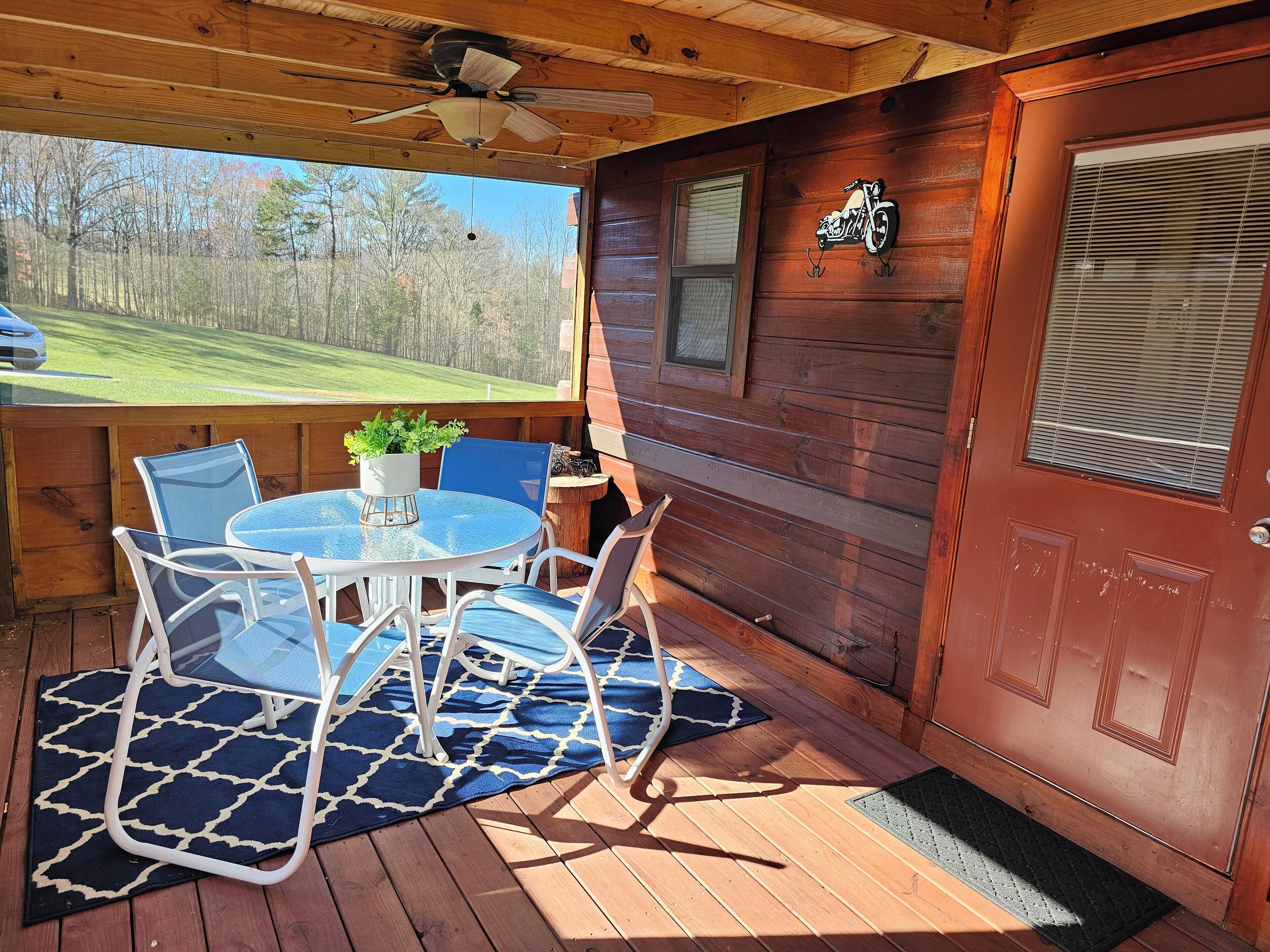 A wooden deck with a table and chairs, a ceiling fan, and a view of a green landscape.