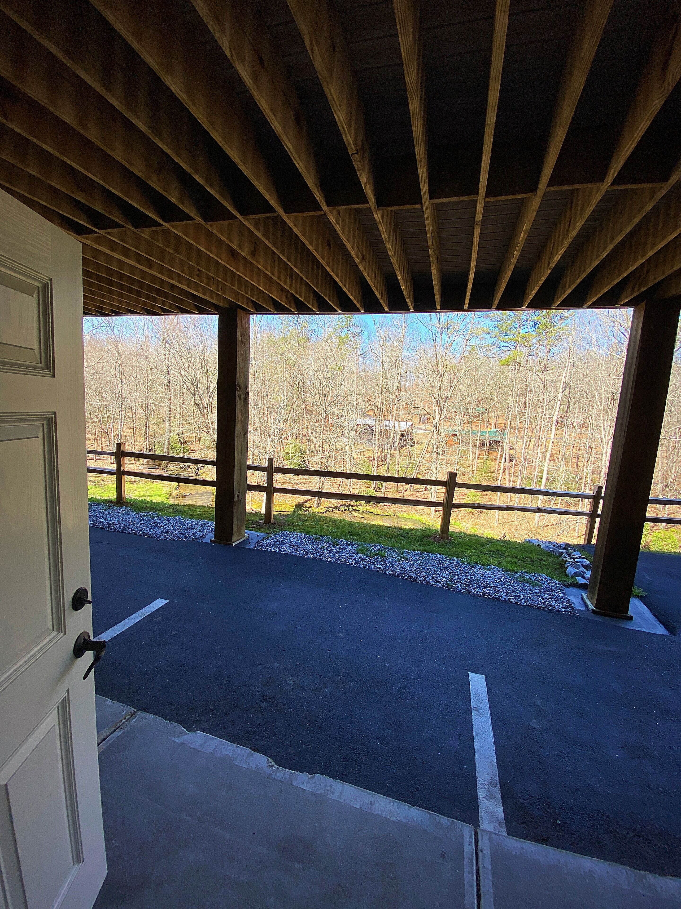 An open doorway leading to a covered outdoor area with a view of a forest and a gravel path.