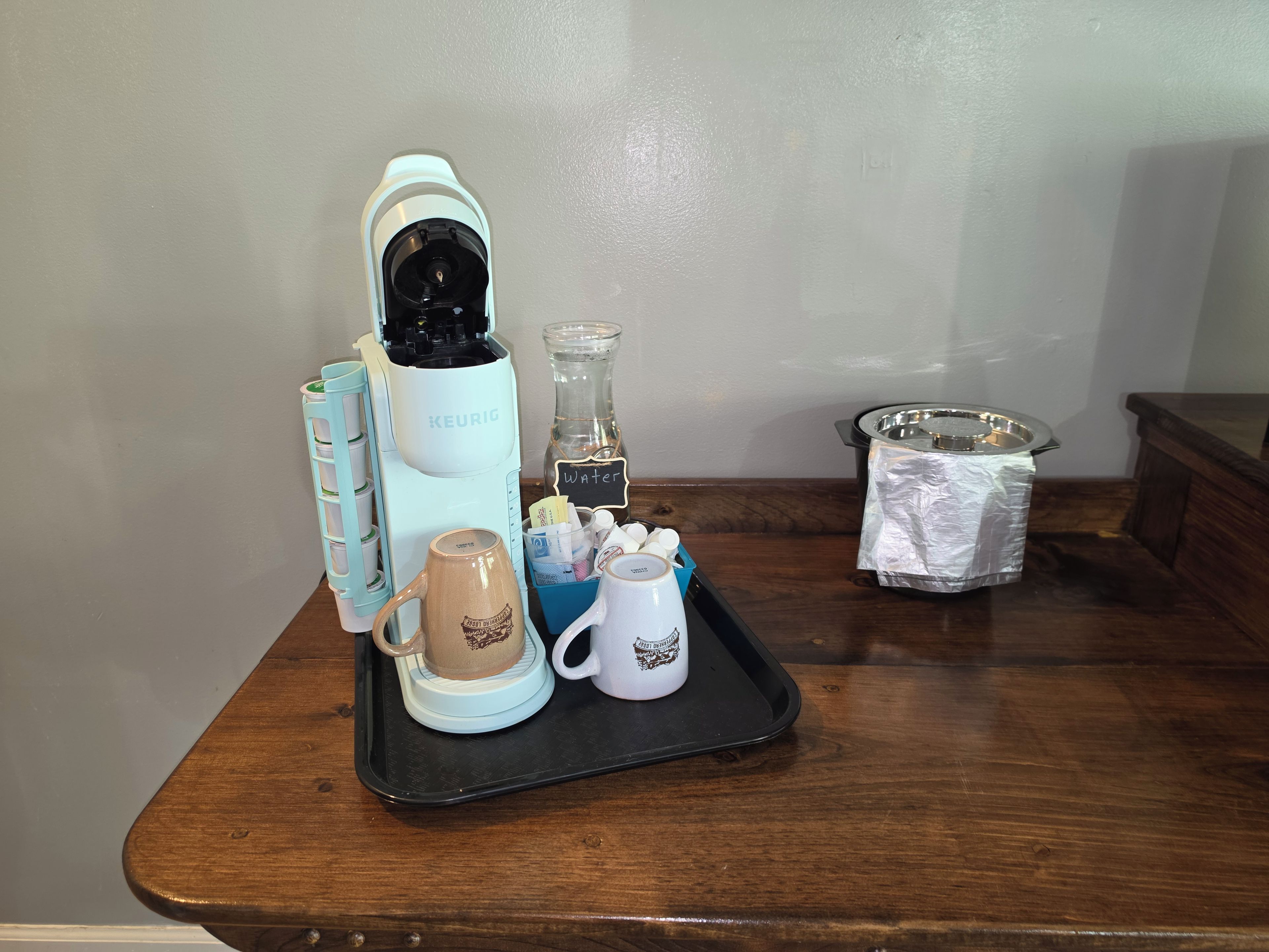 Eine Kaffeemaschine, ein Wasserspender, eine Tasse und ein Tablett auf einem Holztisch.