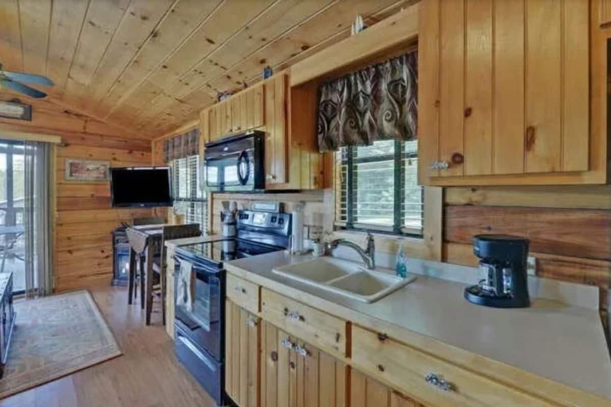 A wooden cabin kitchen with a stove, sink, and a flat-screen TV mounted above the counter.