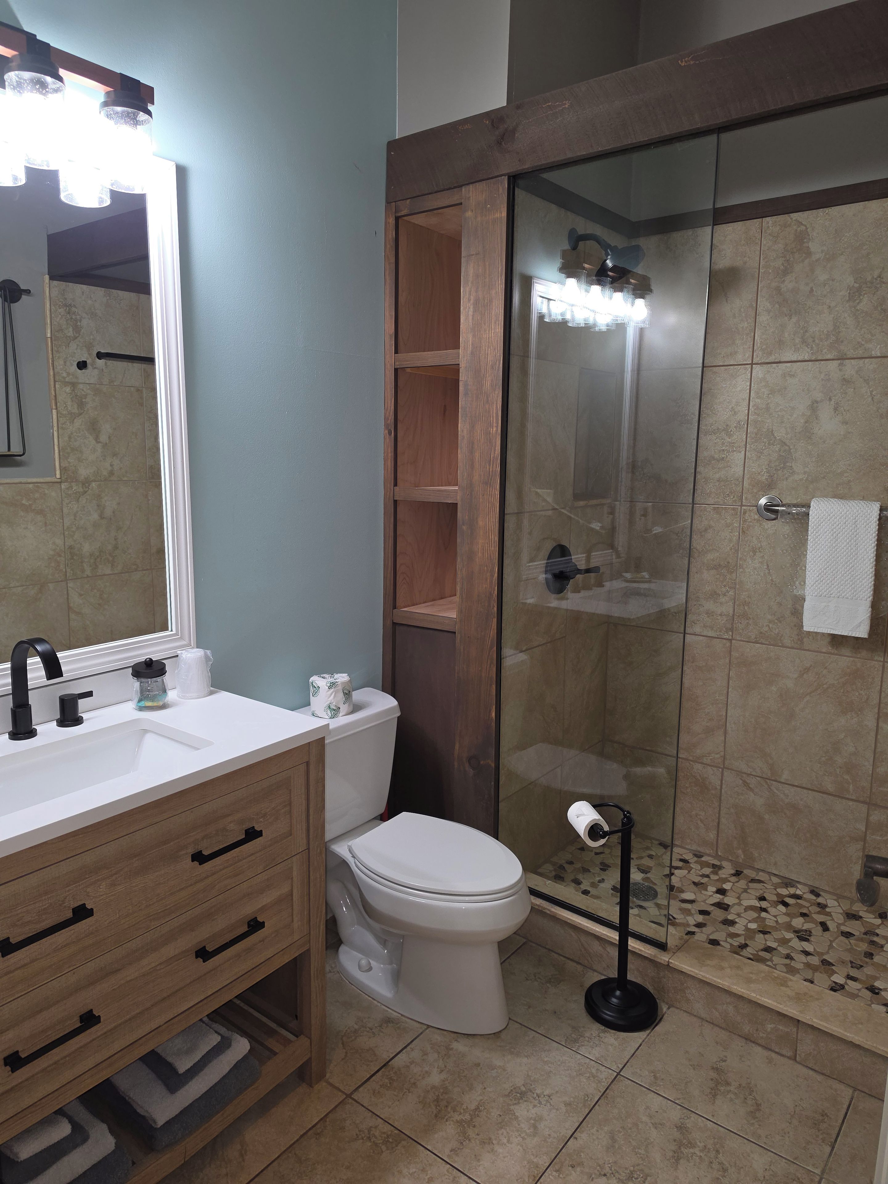 A bathroom with a white sink, wooden vanity, a toilet, and a glass-enclosed shower area.