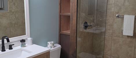 A bathroom with a white sink, wooden vanity, a toilet, and a glass-enclosed shower area.