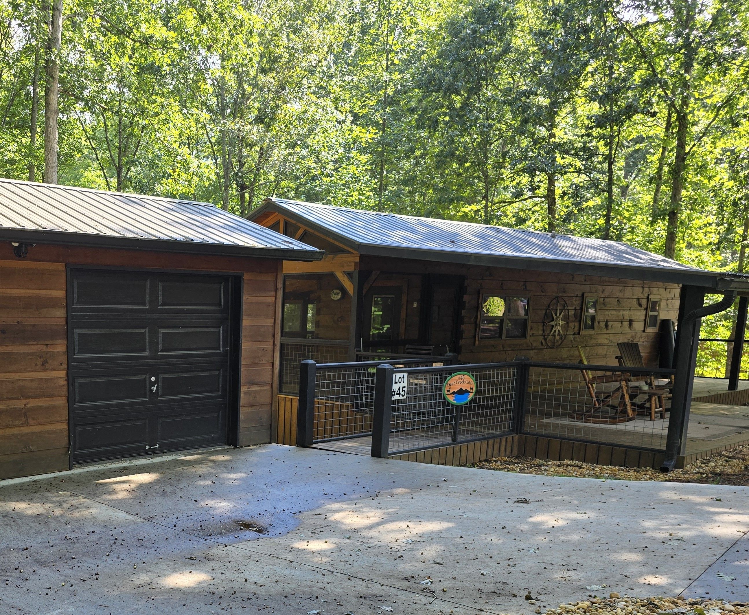 A cabin with a metal roof, a black garage door, and a fenced outdoor area.