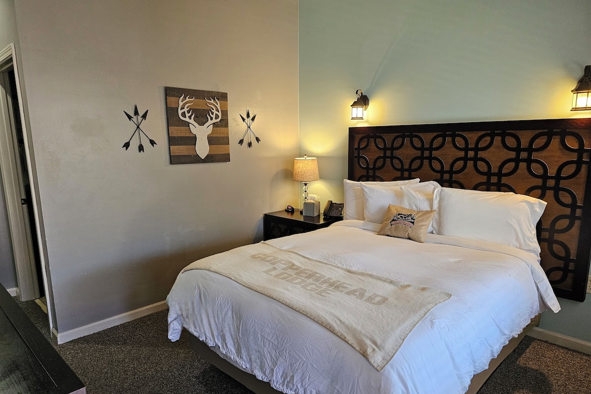 Relax in a serene space with a large bed, wooden headboard, and neutral-toned walls, featuring a deer and arrow wall art.