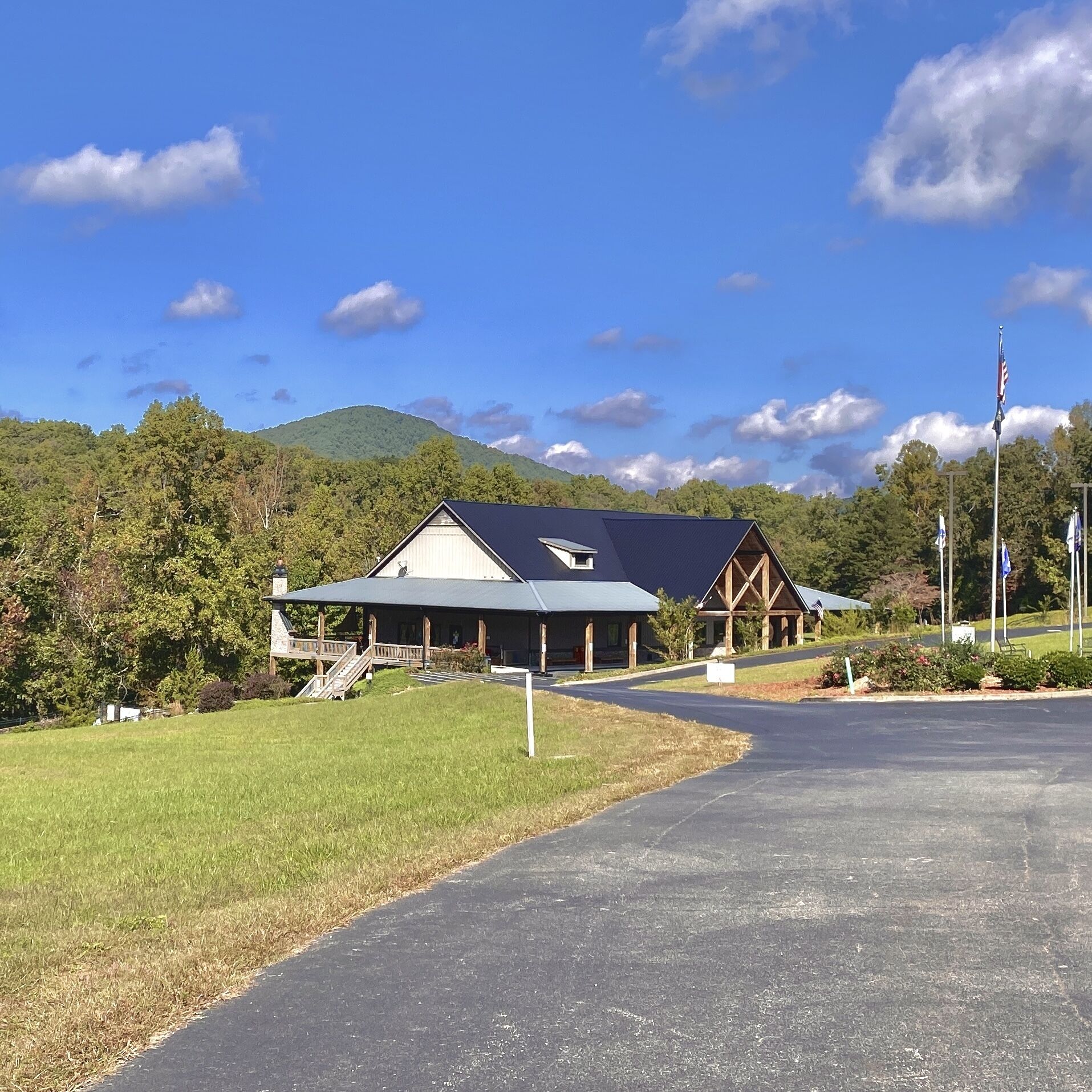 A lodge with a covered porch, a mountain backdrop, and a flagpole.