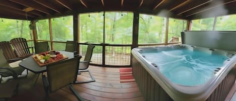 A hot tub area with a table set for a meal, surrounded by chairs, and a view of a forest through large windows.