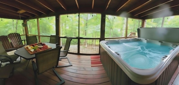 A hot tub area with a table set for a meal, surrounded by chairs, and a view of a forest through large windows. - Copperhead Lodge and Resort Cabin Rentals (Blairsville)