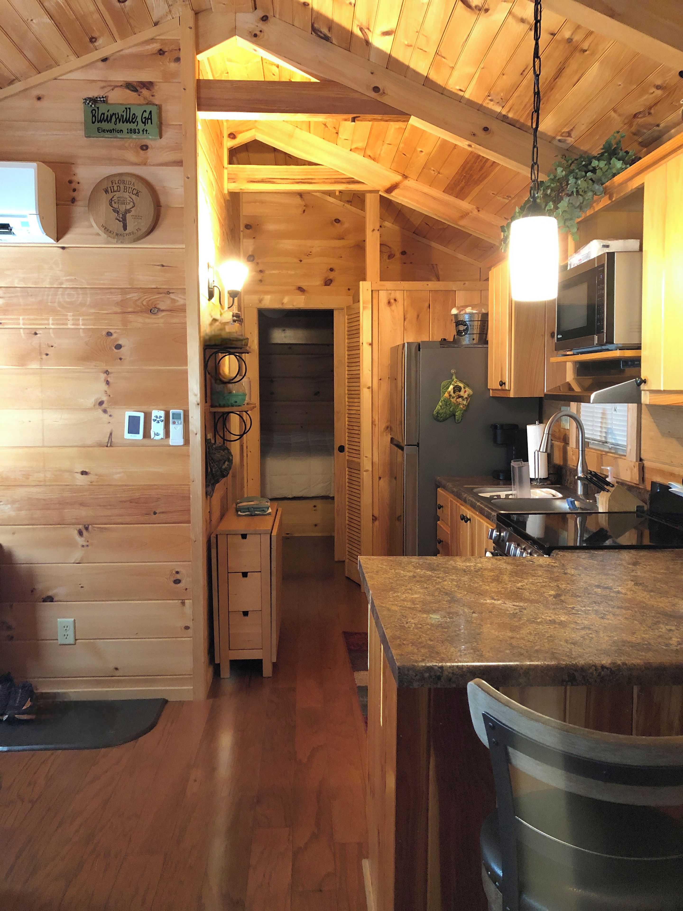 A wooden cabin interior with a kitchen area, a dining table, and a small kitchenette.